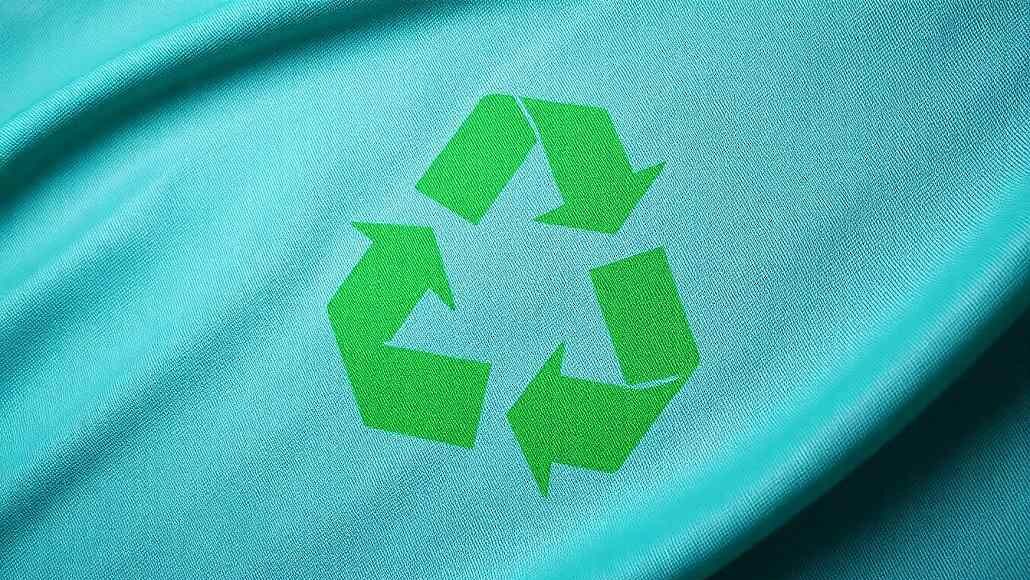 Green recycling symbol printed on turquoise fabric, conveying eco-friendly or recycling theme.