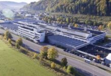 Mayer & Cie. Restarts as Xu Hongjie Reopens Albstadt HQ Aerial view of a large white multi-building campus along a road, with parking and a green field in the foreground and hills in the background.