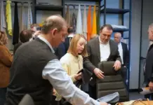 KARL MAYER Enhances Collaboration with Tรผrkiye Customers Group of people in a fabric showroom examining a chair, with fabric swatches on racks in the background.
