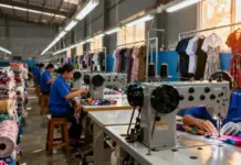 US Manufacturing Output Dips Amidst Shifting Tariff Policies and Persistent Asian Dominance Factory sewing room with workers at sewing machines, stacks of fabric and garments on racks.