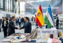 Spain and Uzbekistan Strengthen Textile Industry Ties Two businessmen shake hands at a textile trade fair booth, with fabric samples laid out and flags visible in the background.