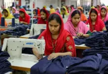 BGMEA and GIZ Sign Sustainable Apparel Pact to Boost Circularity and Decarbonisation Women workers sewing navy fabric on industrial machines in a garment factory; foreground woman in red leads the stitching while others work nearby.