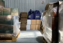 UK Retailers Seek Early End to De Minimis on Low-Value Goods Warehouse storage area with stacked boxes on pallets, plastic wrap, and blue Walter bags in the center.
