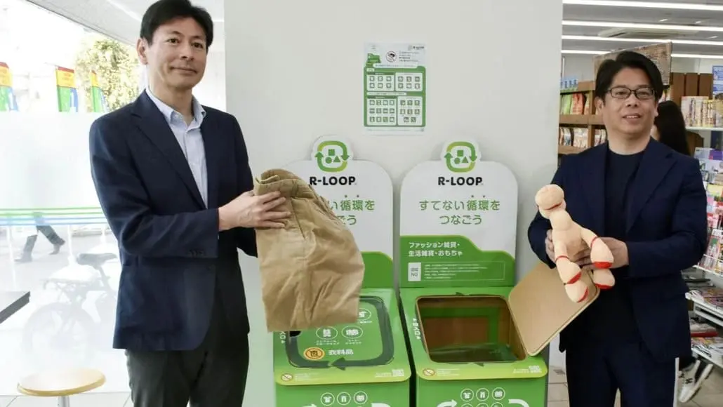 Two men in suits stand beside a green R-LOOP recycling station, each holding recyclable items.