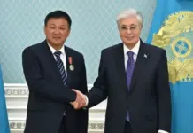 Chinese Company Commits $360 Million to Bolster Kazakhstan’s Cotton Sector Two men in dark suits shake hands in front of blue flags during a formal ceremony, one wearing a medal.