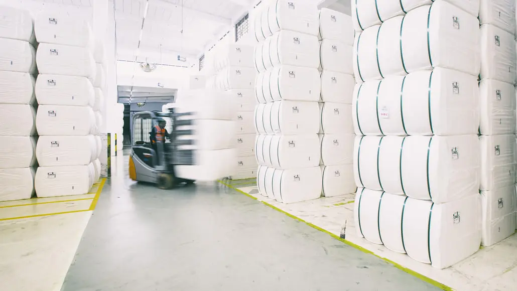 Forklift moving between tall stacks of large white bales in a warehouse mural setting? No, in a warehouse.