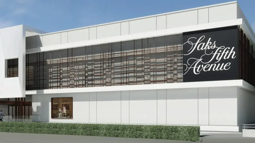 Exterior view of a modern Saks Fifth Avenue storefront with a large black sign reading 'Saks Fifth Avenue' and glass paneling above the ground level.