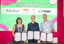 HKRITA, Jeanologia and Looptworks Form Green Machine Circular Textile Ecosystem Three adults stand behind a table, each holding an open certificate during a signing ceremony with a green and pink backdrop.