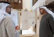 UAE Unveils National Naseej Initiative to Champion Circular Textile Economy Two men in traditional Arabian dress converse in a gallery with display panels and exhibits nearby.