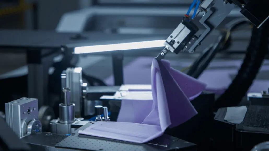 Automated robotic arm handling purple fabric on a manufacturing machine.
