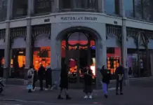 Victoria’s Secret Lifts 2026 Outlook After Strong Q1 Beat Victoria's Secret storefront at dusk with warm orange interior lights and shoppers outside on the sidewalk.