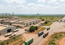 Senate Calls for Total Import Ban to Revitalize Nigeria’s Textile Industry An aerial view of a large factory complex with long warehouses, loading docks, and several trucks on surrounding roads, with a Nigerian flag in the yard.
