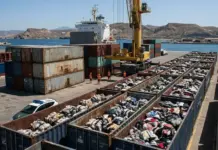 Spanish Court to Hear Alleged Illegal Textile Waste Import Case Port scene with stacked shipping containers, a large crane, and rail-cars filled with clothing beside the water.