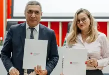 Uzbekistan and Poland Forge Stronger Textile and Light Industry Ties Two professionals in a conference room pose with signed documents in front of a red and white backdrop, facing the camera.
