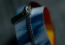 YKK Unveils EXCELLA® Zipper Concept Utilizing Recycled Nonwoven Fabric in Japan and France Close-up of a metal zipper slider on blue fabric with a rainbow-colored edge.