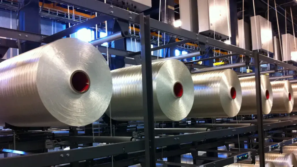 Row of large silver rolls with red cores on a metal conveyor rack in a factory setting.