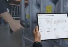 Shinwon Implements AI and Blockchain for Full Raw Material Traceability Person scanning with a handheld barcode scanner while holding a tablet showing a supply chain traceability dashboard in a warehouse voyage area.