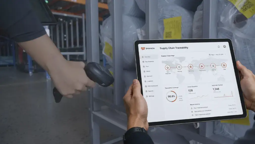 Person scanning with a handheld barcode scanner while holding a tablet showing a supply chain traceability dashboard in a warehouse voyage area.