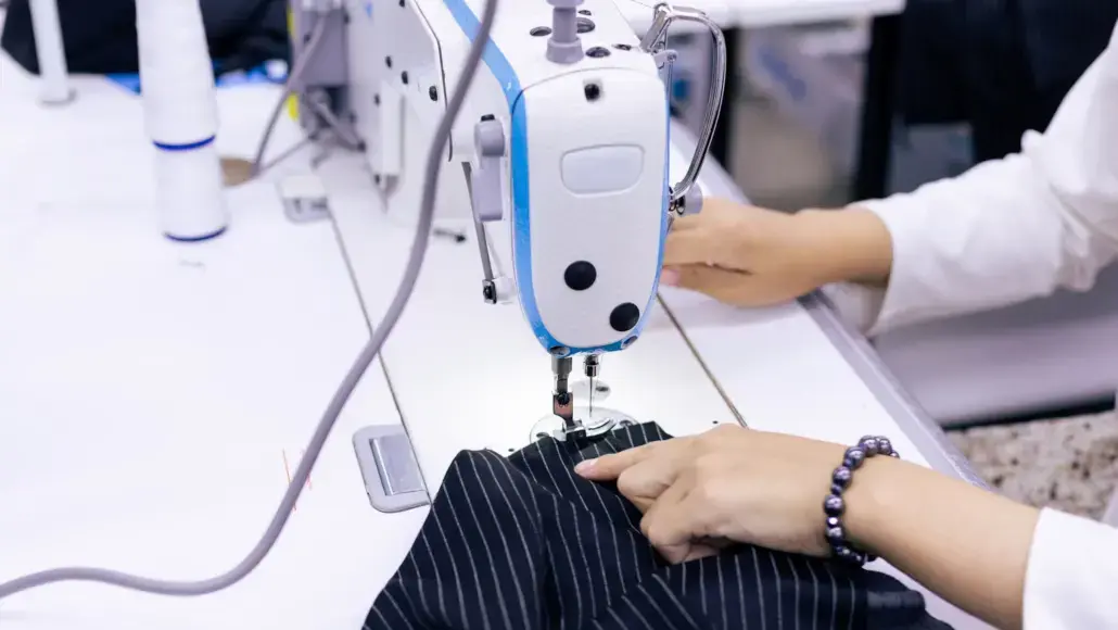 Person sewing dark pinstriped fabric with an industrial sewing machine.