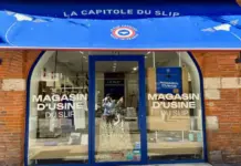 Le Slip Français Lists in Paris to Boost French Apparel Production Blue awning storefront for La Capitole du Slip, brick facade and glass doors with 'MAGASIN D'USINE DU SLIP' text on the windows/doors as a factory outlet shop sign.