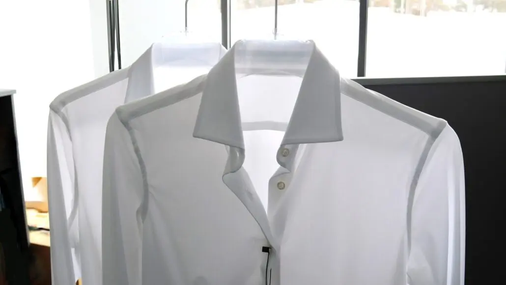 White dress shirt on a hanger in a shop, front view with collar and buttons visible near a window.