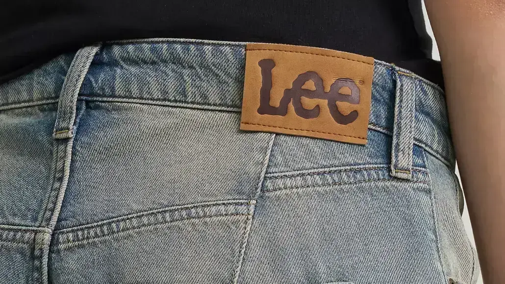 Close-up of blue denim jeans waistband with a brown Lee brand patch above the back pocket area.
