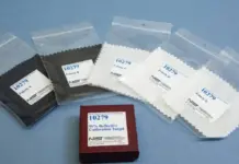 NIST Introduces New Reference Material to Standardize Textile Fiber Identification Set of calibration targets in sealed bags (black and white) with a red box labeled '10279 99% Reflective Calibration Target' on a blue surface.