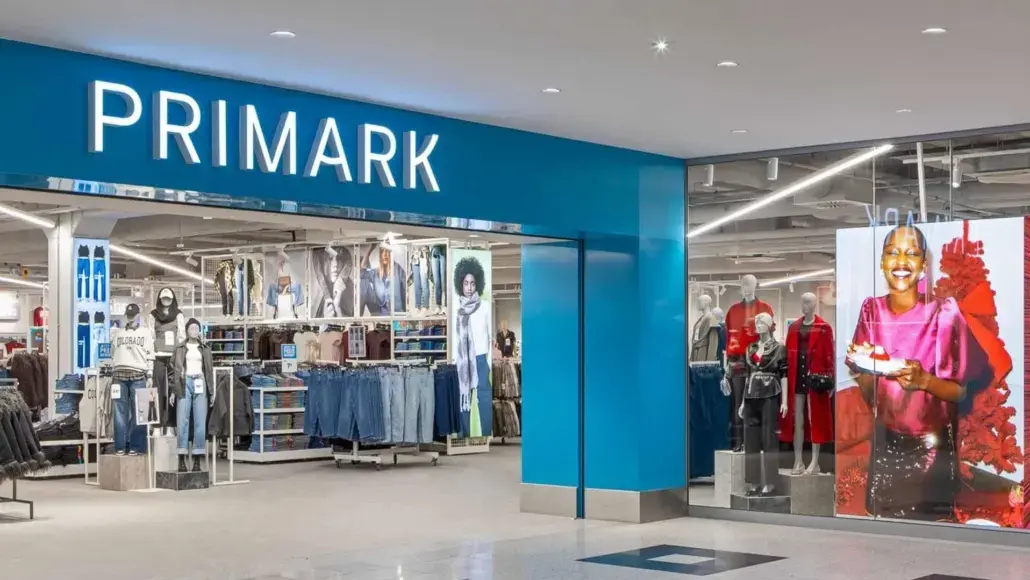 Front of a Primark store with a bright blue sign and visible clothing racks inside the entrance.