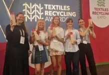Textile Recycling Awards Showcase Industry Champions in Brussels Six women posing on a stage at a Textiles Recycling Awards event, each holding a tall wooden trophy in front of a blue and red backdrop reading 'Textiles Recycling Awards'.