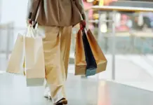 Joor Data Analyzes Post-Brexit Trade Patterns Across European Fashion Markets Person in a tan suit walks through a shopping mall carrying multiple shopping bags in each hand.