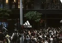 Adidas Achieves Record Quarterly Revenue in Q2 2026 Crowd of people wearing masks gathered outside an Adidas storefront with large logo signs.