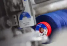 Coats PLC Navigates Market Headwinds with Resilient H1 2026 Financial Performance Close-up of a blue COATS Epic thread spool on a sewing machine being wound onto a spindle.