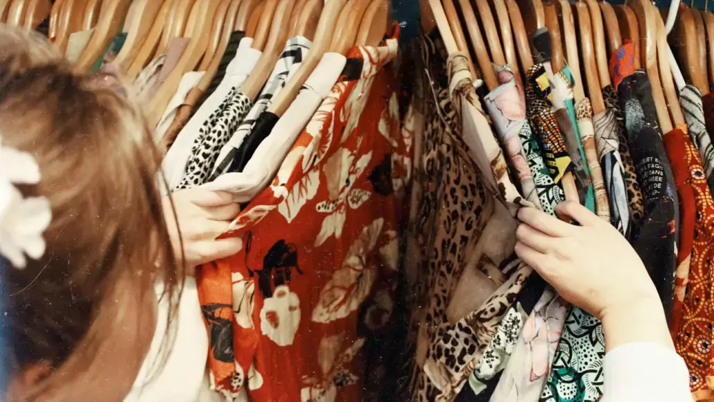 People browsing a clothing rack with colorful patterned dresses on wooden hangers, selecting fabrics with their hands