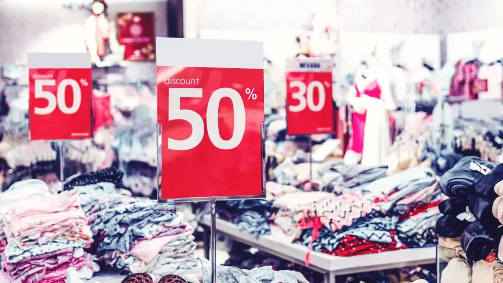 Clothing store with bright red 50% off signs indicating discounts on apparel stacks and mannequins in background