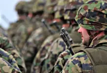 Fashion Roundtable Urges Strategic Shift to UK Textile Manufacturing Soldier in camouflage uniform and helmet with a rifle, standing among other soldiers in a field formation.