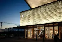 LVMH Reports Strong H1 2026 Results as Fashion Sales Rebound Louis Vuitton storefront at dusk with a lit patterned façade and shoppers entering the glass doors.