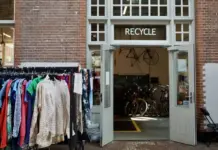 UK Sustainable Fashion Reaches £13.7 Billion Valuation Driven by Secondhand Expansion Open storefront with a 'RECYCLE' sign; clothes on racks outside and bicycles visible inside the shop.