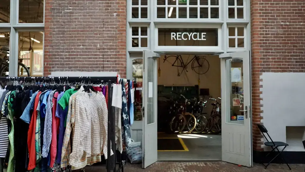 Open storefront with a 'RECYCLE' sign; clothes on racks outside and bicycles visible inside the shop.