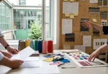 Cascale and Textile Exchange Enhance Supply Chain Taxonomy Two designers discuss fabric swatches and color samples on a bright studio table with notes and a corkboard in the background.