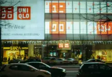 Fast Retailing Lifts FY26 Forecast After Record Nine-Month Growth UNIQLO storefront at night with large orange logo, LifeWear banner, and string lights; busy street with cars in foreground.