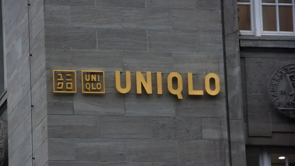Golden UNIQLO sign on a gray stone building exterior, with the brand name spelled in large letters and two square logos to the left