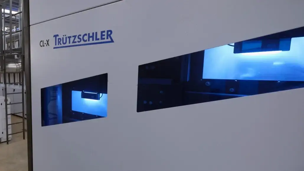 Industrial textile machine with the Trützschler CL-X logo visible and blue-lit viewing windows on the side panel