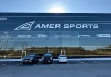 Amer Sports Posts 339% Operating Profit Surge in Q2 on Salomon and Arc’teryx Momentum Facade of the Amer Sports building with a large logo and brand logos (Arc'teryx, Salomon, Wilson, PeakPerformance, Atomic, Armada) and three cars parked in front.