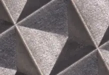 Luxinar Scales Operations to Meet Femtosecond Laser Demand Close-up of a geometric textured wall with interlocking triangular facets in gray tones.