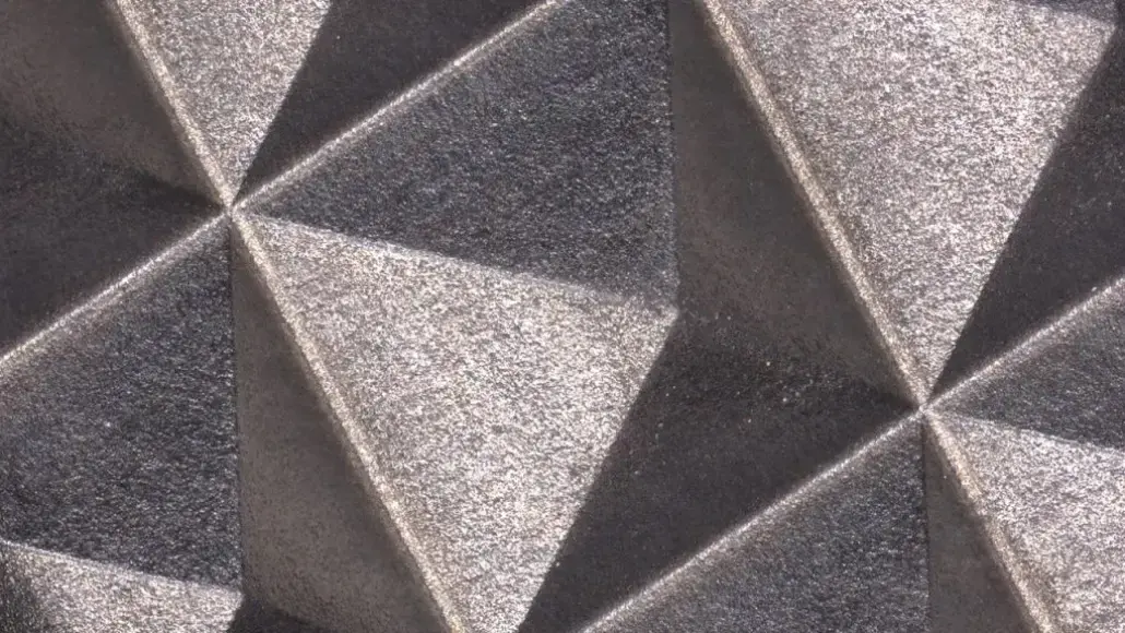 Close-up of a geometric textured wall with interlocking triangular facets in gray tones.