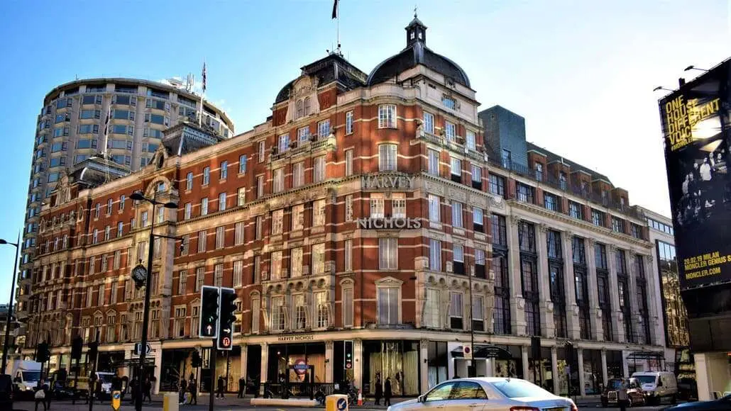 Harvey Nichols department store on a busy city street, red-brick facade and pedestrians nearby.