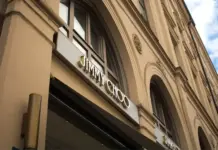 Capri Holdings Reports Lower Q1 FY27 Revenue, Cuts Outlook Jimmy Choo storefront on a beige historic building with arched windows and a large sign above the entrance.