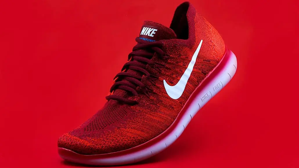 Red Nike running shoe with white swoosh on a red background, angled to show the side and sole edge.