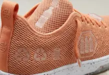 Karl Mayer Inaugurates New Textile Innovation Center to Drive Footwear Advancements Close-up of a peach-colored mesh running shoe featuring recycled-material symbols and a speckled white sole on the heel side edge.