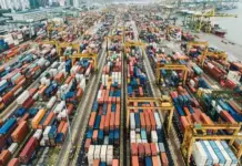 Pakistan Exports Increase to $2.96 Billion in Opening Month of Fiscal Year Aerial view of a shipping container yard with colorful containers and yellow gantry cranes at a busy port.